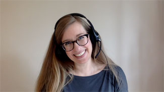 Smiling woman with headset and glasses in front of a tan background